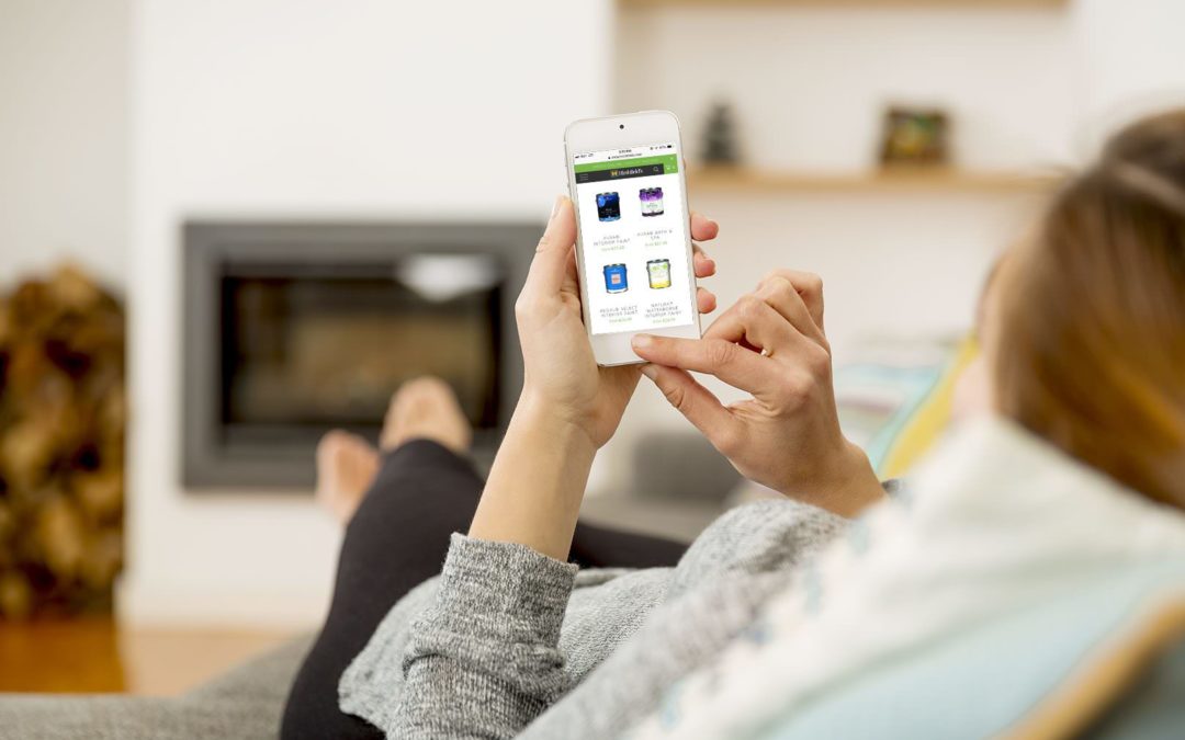 A female lying on a couch shopping online for paint through her mobile phone.