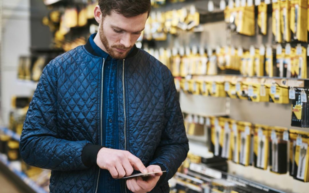 A man shopping at a hardware store, reading the back of a package.